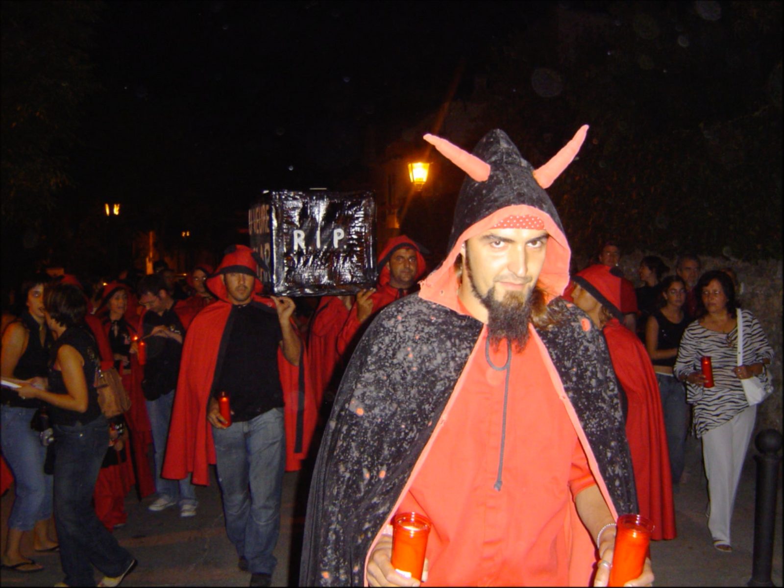 Un diable amb caputxa de banyes i ciris vermells durant la cercavila de dol